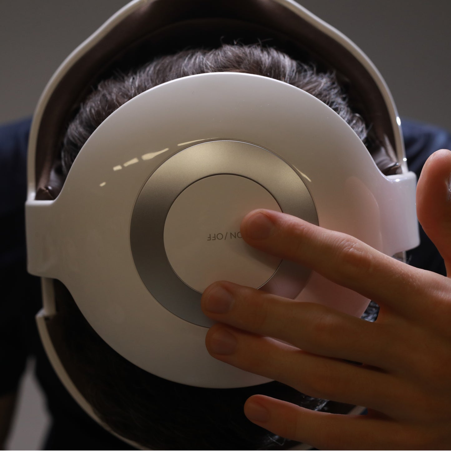 Breo iDream 5S head massager. White design, hand pressing the On/Off button for eye strain relief.