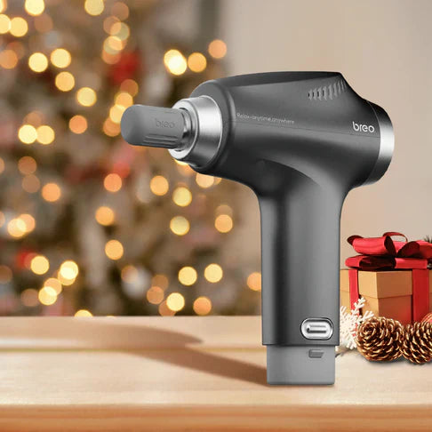 A close-up of a black Breo massage gun on a wooden table, with a Christmas tree and a gift in the background