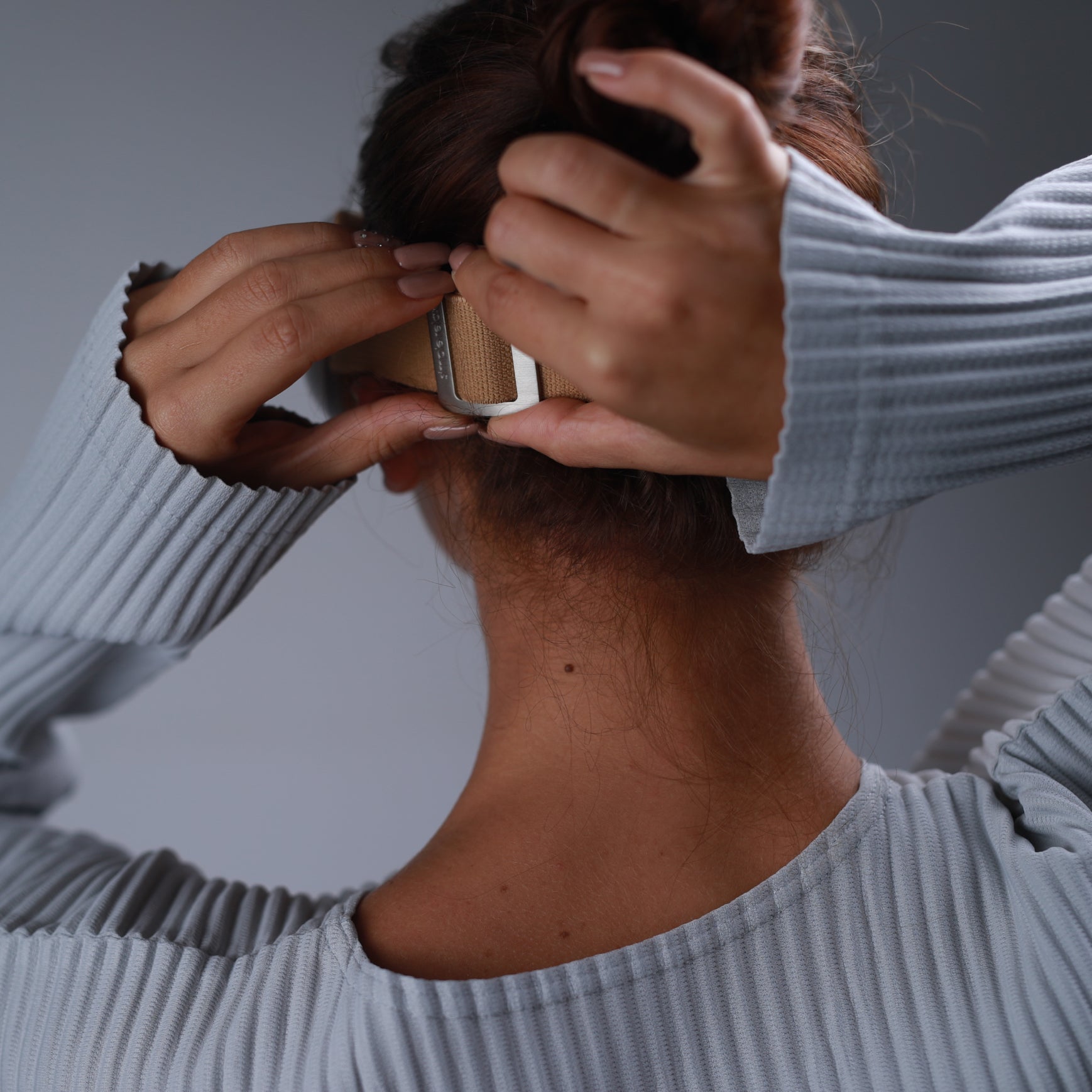 Woman adjusting Breo iSee4 Eye Massager, focus on the strap detail. Beige strap, silver buckle, eye strain relief product.